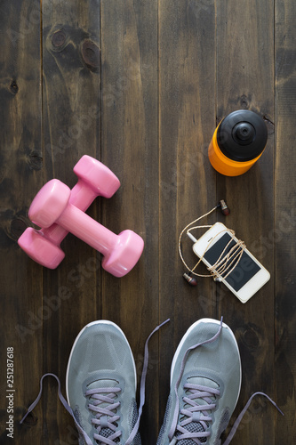 Fototapeta Naklejka Na Ścianę i Meble -  Fitness, healthy and active lifestyles Concept, dumbbells, running shoes, bottle of water, smartphone with earphone on wooden background. Top view with copy space for text.