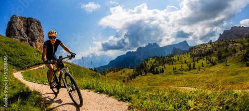 Fototapeta Naklejka Na Ścianę i Meble - Tourist cycling in Cortina d'Ampezzo, stunning Cinque Torri and Tofana in background. Man riding MTB enduro flow trail. South Tyrol province of Italy, Dolomites.