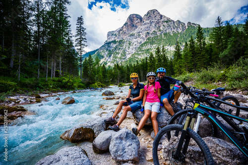 Tourist cycling in Cortina d'Ampezzo, stunning rocky mountains on the background. Family riding MTB enduro flow trail. South Tyrol province of Italy, Dolomites. photo