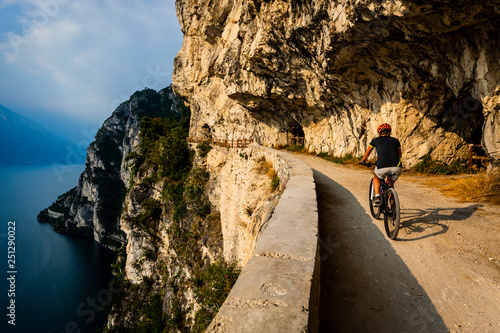 Cycling woman  riding on bikes at sunrise mountains and Garda lake landscape.  Cycling MTB enduro flow sentiero ponale trail track. Outdoor sport activity.