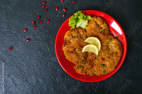 Φωτογραφία Large Viennese schnitzel on a red plate with lemon on a black background
