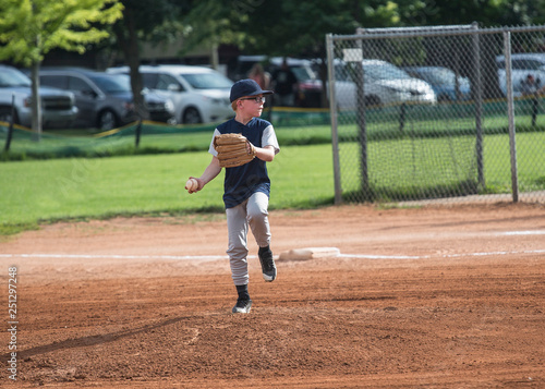 Full length Action photo of a Little League baseball pitcher throwing a pitch. Young boy with glasses focused on winning