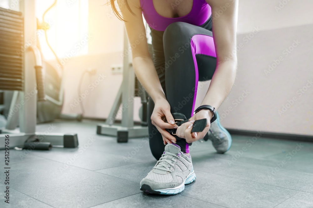 Young woman wearing leather ankle straps prepares to exercise on fitness machine in the gym. Fitness, sport, training, people concept. Young woman wearing leather ankle straps prepares to exercise on fitness machine in the gym. Fitness, sport, training, people concept.
