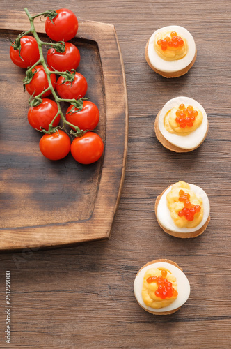 Board with tasty deviled eggs and tomatoes on wooden table