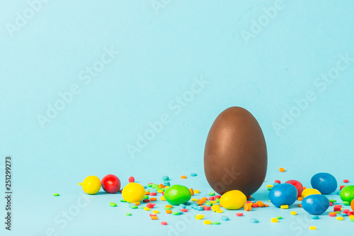 Chocolate Easter egg and multi-colored sweets on a blue background. Easter celebration concept