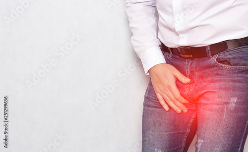 A man in a white shirt holding his groin with an infection and prostatitis, urology, copy space, inflammation photo