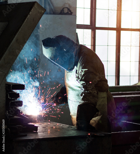 Welder at the factory in a welding mask welds metal parts, welding and sparks, industrial