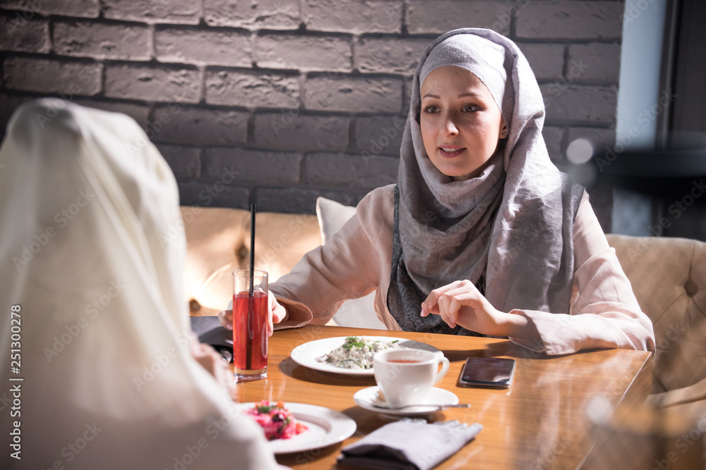 Two Muslim women chatting at a table in a restaurant Two Muslim women chatting at a table in a restaurant