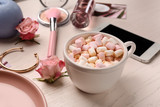 Cup of hot cacao with marshmallows and female accessories on white table