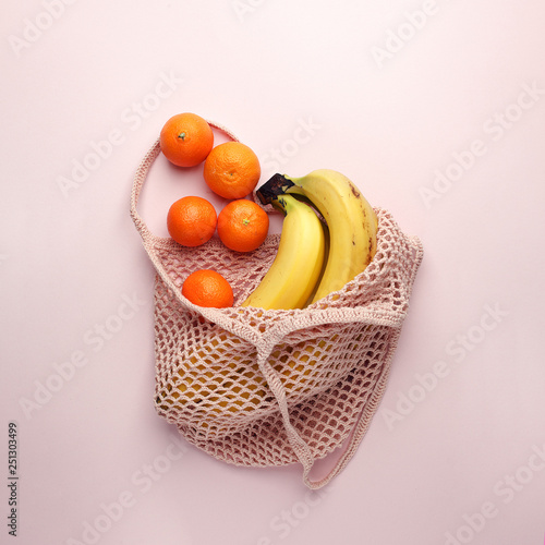 Mesh shopping bag with exotic fruits on pink canvas background. Summer time blogger organic food concept, minimal
