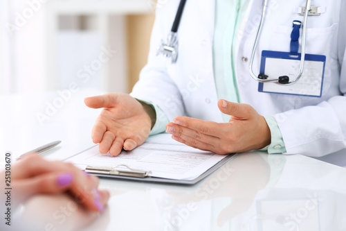 Unknown doctor and patient talking while sitting at the desk in hospital office  close-up of human hands. Medicine and health care concept