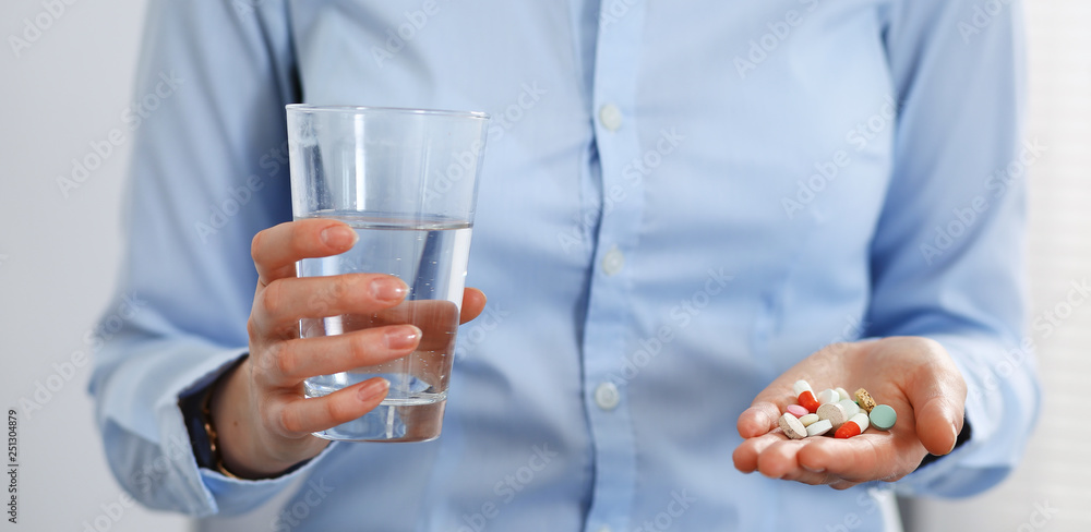 Young unknown woman holding pills and glass of water, closeup of hands. Medicine and healthcare concept Young unknown woman holding pills and glass of water, closeup of hands. Medicine and healthcare concept