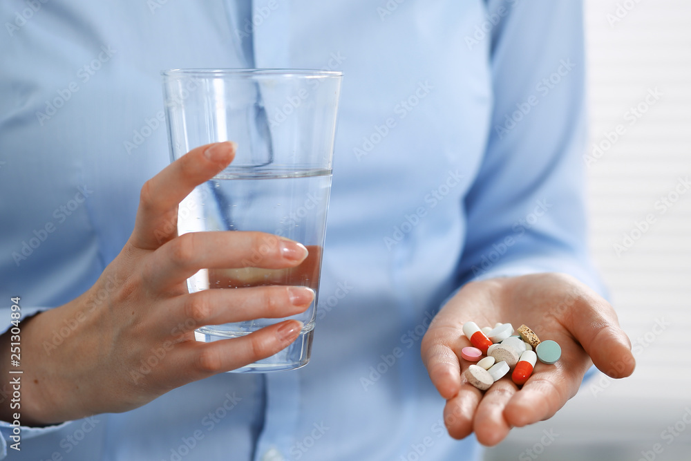 Young unknown woman holding pills and glass of water, closeup of hands. Medicine and healthcare concept Young unknown woman holding pills and glass of water, closeup of hands. Medicine and healthcare concept