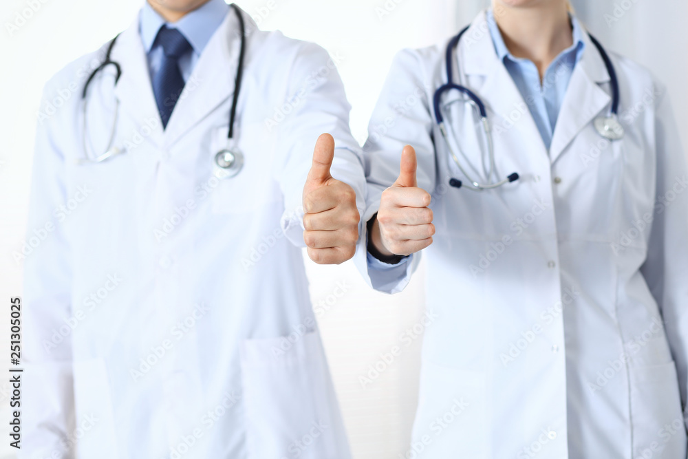 Team of unknown medicine doctors showing OK sign with thumb up close up. Success and high level service in health care, best treatment and customer loyalty and physical concept Team of unknown medicine doctors showing OK sign with thumb up close up. Success and high level service in health care, best treatment and customer loyalty and physical concept
