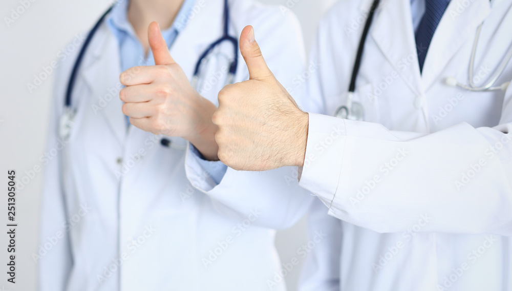 Team of unknown medicine doctors showing OK sign with thumb up close up. Success and high level service in health care, best treatment and customer loyalty and physical concept Team of unknown medicine doctors showing OK sign with thumb up close up. Success and high level service in health care, best treatment and customer loyalty and physical concept