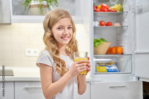 Pretty girl holding glass with orange juice and smiling.