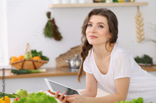 Young woman looking for a new recipe for cooking in a kitchen. Housewife is making online shopping by tablet computer and credit card