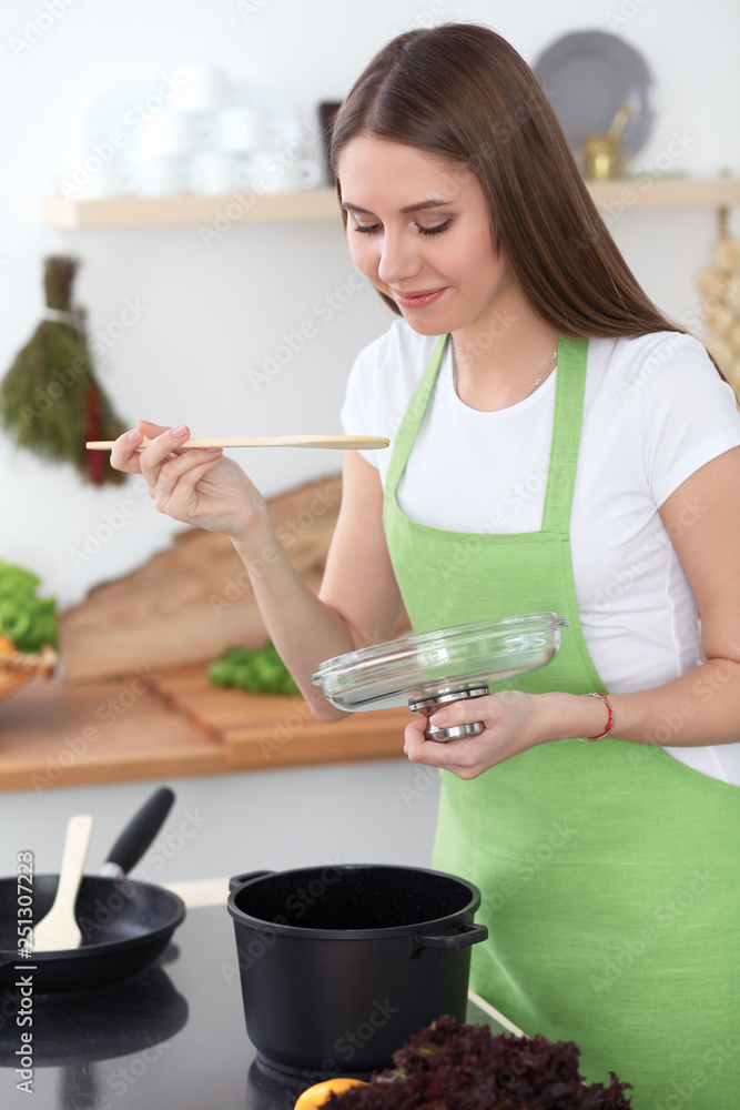 Young happy woman cooking soup in the kitchen. Healthy meal, lifestyle and culinary concept. Smiling student girl preparing vegetarian meal at home Young happy woman cooking soup in the kitchen. Healthy meal, lifestyle and culinary concept. Smiling student girl preparing vegetarian meal at home