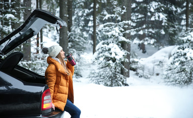 Young woman with hot drink near car at winter resort