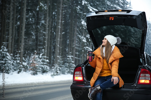 Young woman with hot drink near car at winter resort