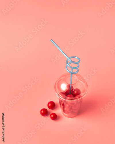 Fresh organic cherry tomatoes in a plastic cup with blue straw on a color background of the year 2019 Living Coral Pantone. Copy space. Natural fresh juice.