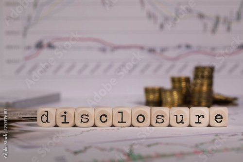 Word DISCLOSURE composed of wooden letter. Stacks of coins in the background.