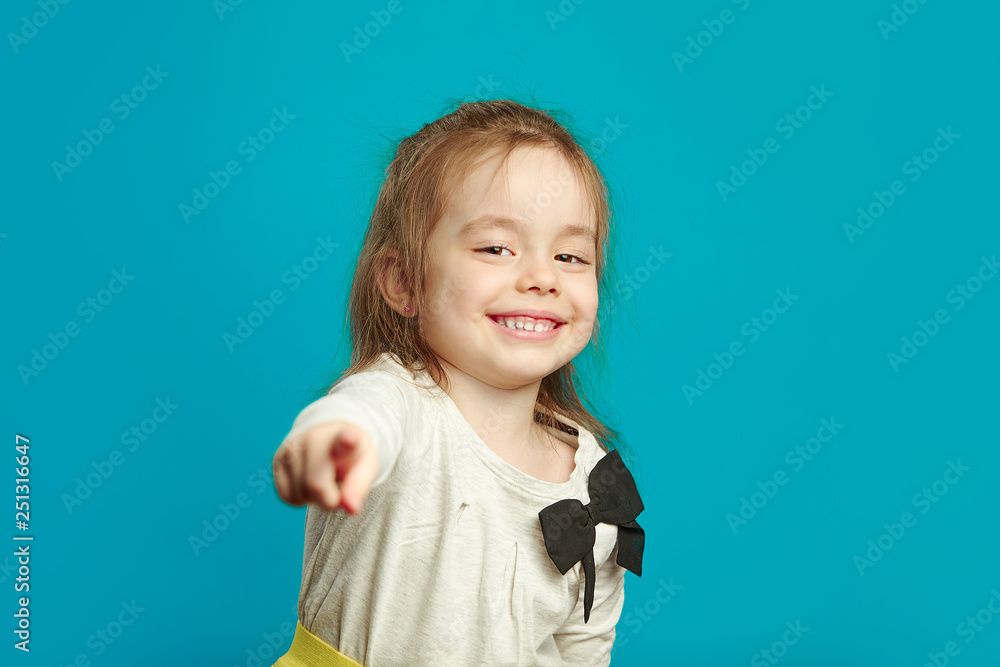 Little smiling girl is points her finger on you over blue isolated background. Little smiling girl is points her finger on you over blue isolated background.