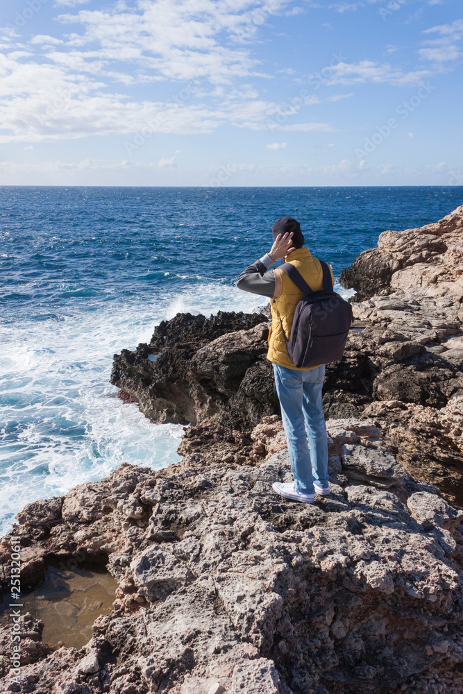 man tourist in yellow vest with backpack on rock cliff in Malta