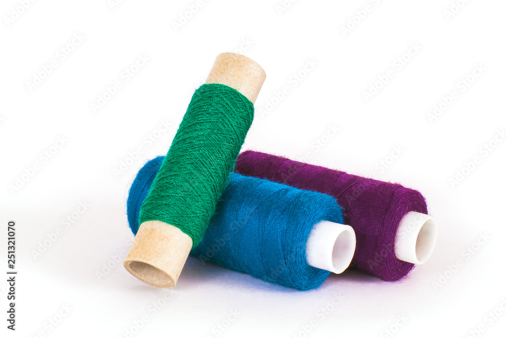 Blue, green and purple sewing threads on white background