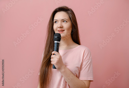 young woman with microphone in hand on pink background