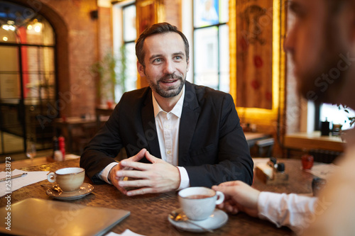 Portrait of handsome mature  businessman talking to partner during meeting in cafe, copy space