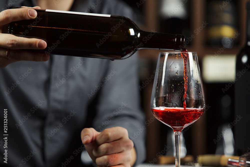 Fototapeta premium Close up shot of sommelier pouring red wine from bottle in glass