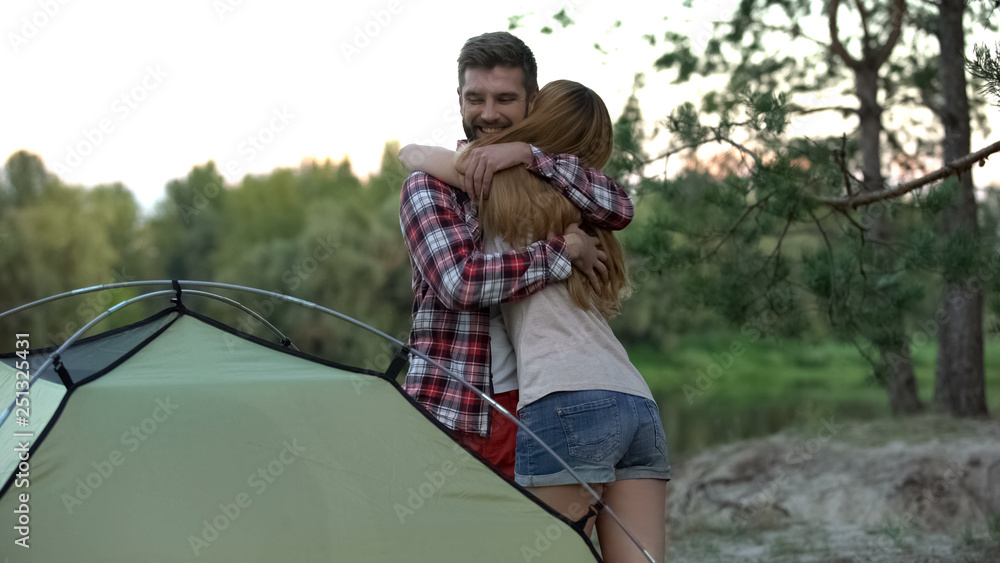Obraz premium Couple embracing, putting up tent, great teamwork, wilderness survival school
