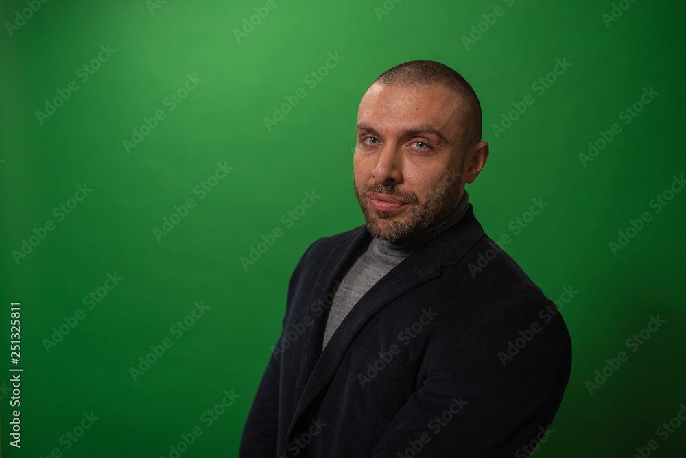 Fototapeta premium Studio fashion portrait in monochrome. Elegant young handsome serious man iin studio with green background.