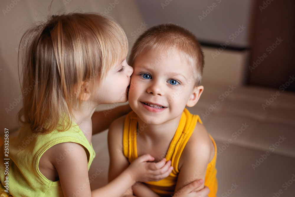 cute smiling children, brother and sister, 2-3 years old, pogodki, a girl in a tutu skirt, dressed in bright yellow colors playing on the couch and hugging cute smiling children, brother and sister, 2-3 years old, pogodki, a girl in a tutu skirt, dressed in bright yellow colors playing on the couch and hugging