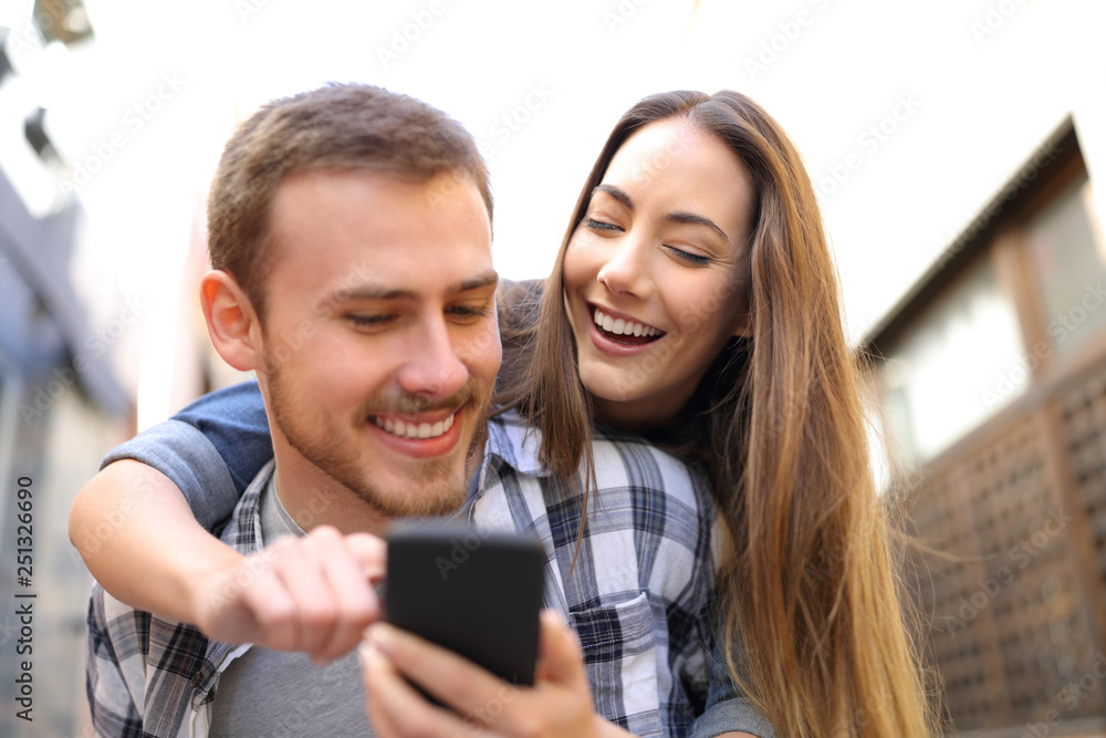 Happy couple piggybacking checking smart phone