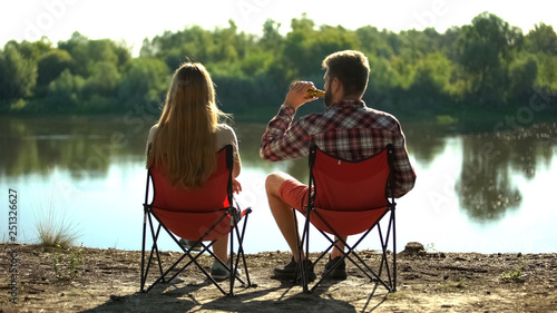 Couple sitting and enjoying beautiful river scape, man drinking beer, addiction