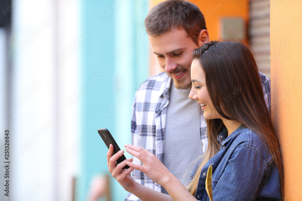 Happy couple browsing smart phone content in the street Happy couple browsing smart phone content in the street