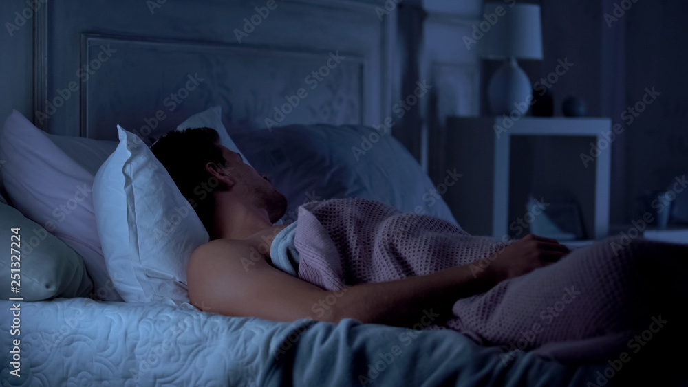 Man deeply sleeping on bed in dark room, comfortable mattress and pillows, dream Man deeply sleeping on bed in dark room, comfortable mattress and pillows, dream