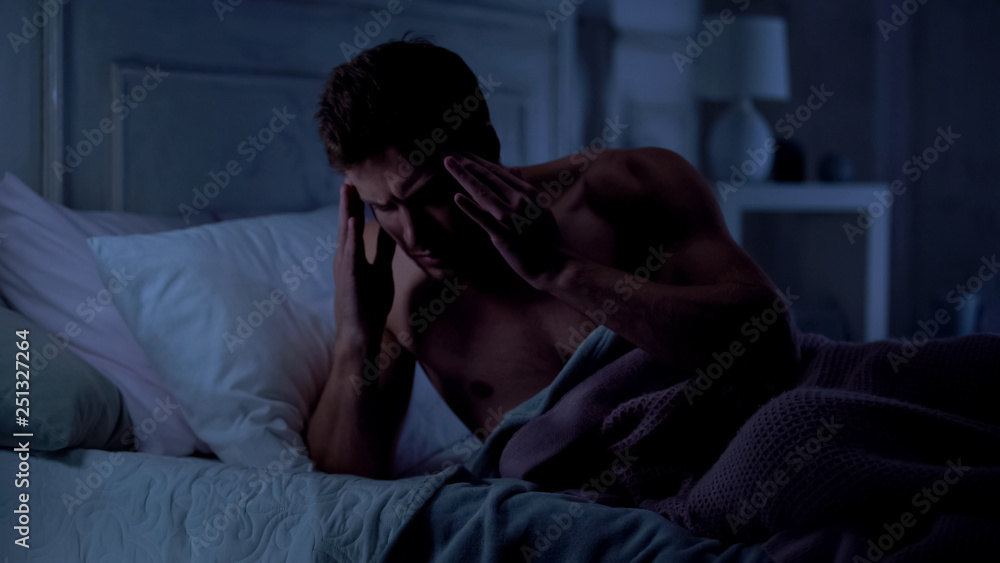 Fototapeta premium Young man suffering migraine, rubbing his temples, having bad sleep, stress