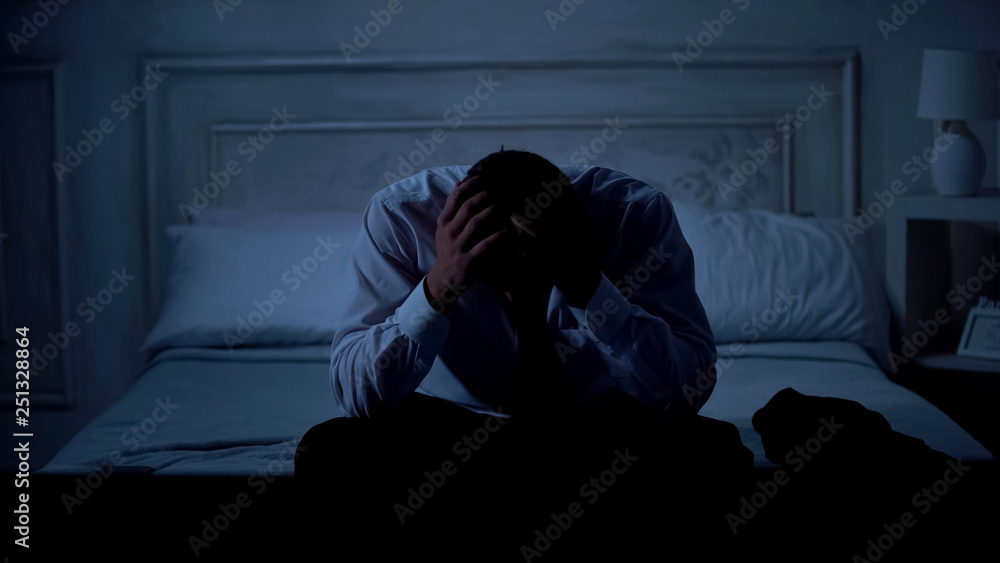 Unhappy businessman sitting on bed, project failure, unemployment and bankruptcy