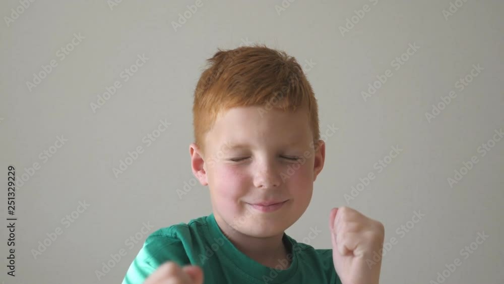Adorable handsome boy raising hands and dancing rejoicing achievement. Portrait of child with freckles. Happy young kid closed his eyes enjoying the dance indoor. Slow motion Close up Adorable handsome boy raising hands and dancing rejoicing achievement. Portrait of child with freckles. Happy young kid closed his eyes enjoying the dance indoor. Slow motion Close up