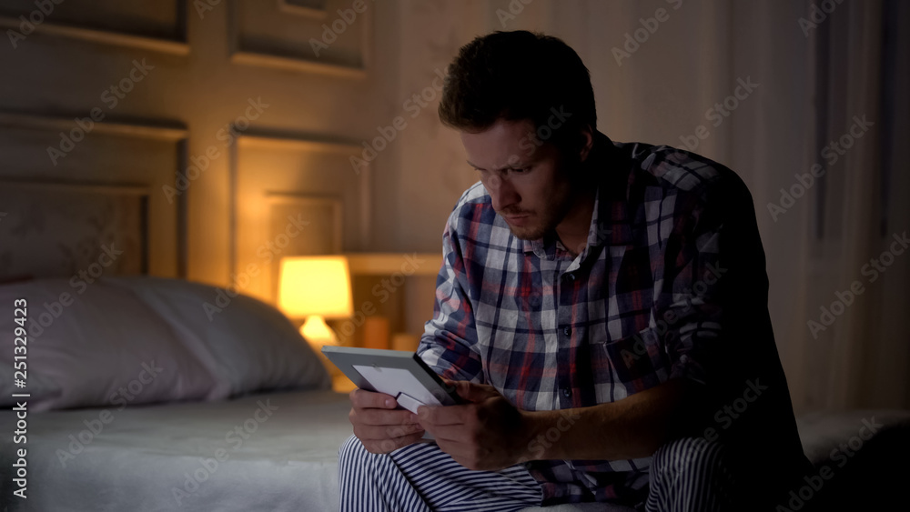 Unhappy lonely young male sitting on bed looking at photo, breakup, missing wife