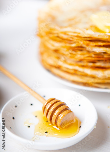 A stack of thin russian pancakes with butter and honey on a white plate