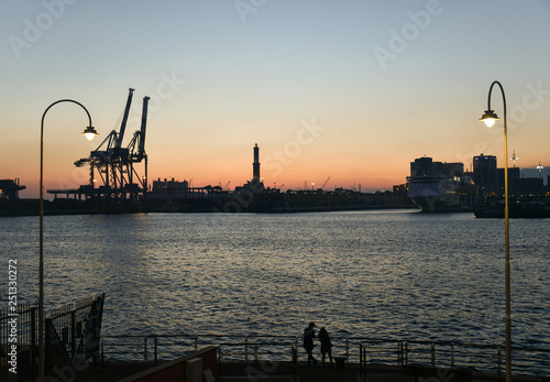 Elevated view of the Old Port (Porto Antico) with the silhouette of the Lighthouse (Faro di Genoa but simply called Lanterna), a symbol and landmark of the city, at sunset photo