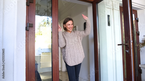 Obraz na plátně Mother standing by door and waving hand to children walking to school, goodbye