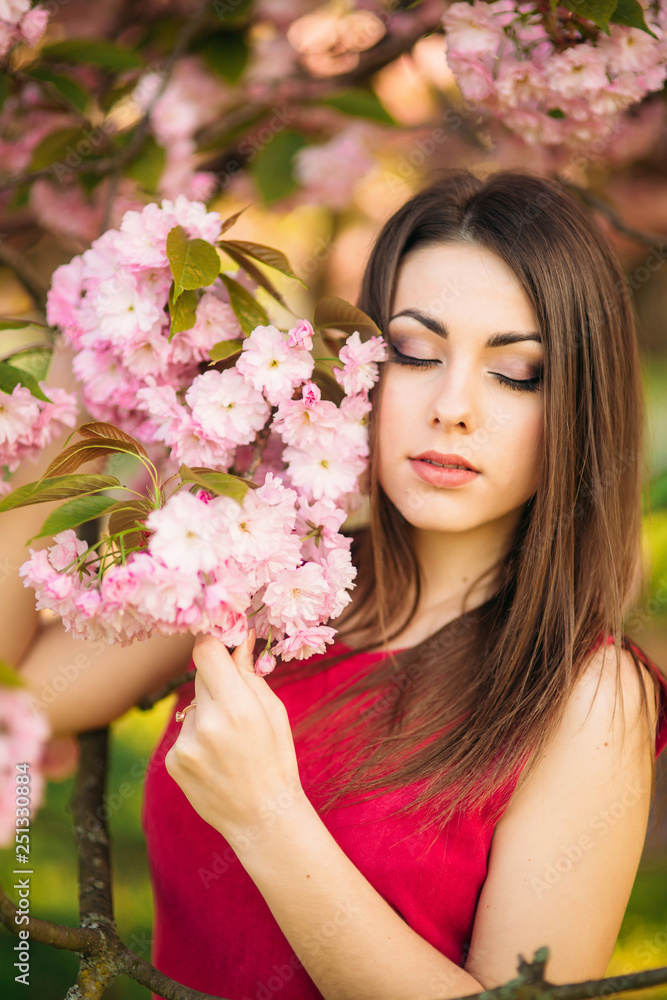 Portrait of beutiful girl in sakura tree. Sakura flowers surround the girl. Sakura branch by her face Portrait of beutiful girl in sakura tree. Sakura flowers surround the girl. Sakura branch by her face