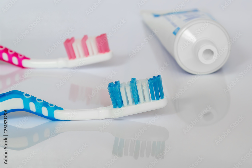 Two toothbrushes and toothpaste on a white glossy background. The concept of daily dental care Two toothbrushes and toothpaste on a white glossy background. The concept of daily dental care