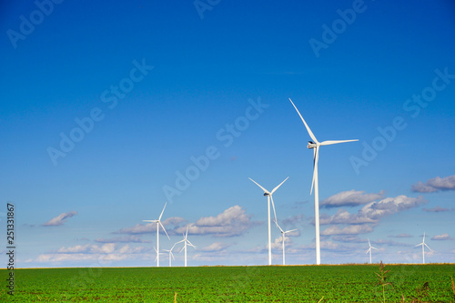 wind power plant consisting of several wind turbines standing in a field against a blue sky