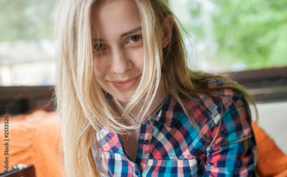 A girl with beautiful eyes, in a plaid shirt, sits in a summer cafe against the background of large glass windows. The look of the girl is directed directly to the camera. A girl with beautiful eyes, in a plaid shirt, sits in a summer cafe against the background of large glass windows. The look of the girl is directed directly to the camera.